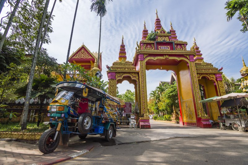 Un taxi de moto tuk tuk junto a un templo en Vientiane, Laos.