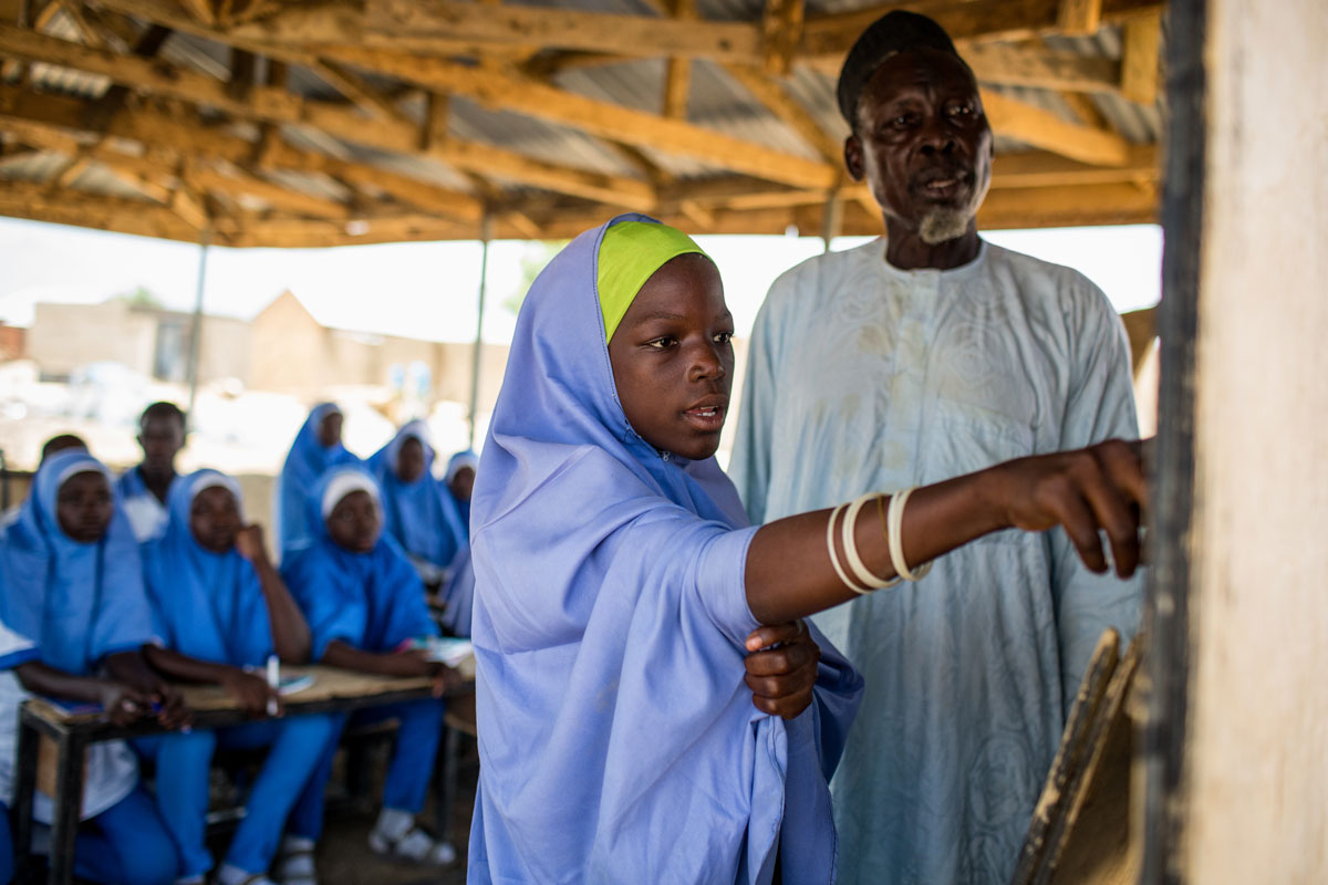Nigeria: In the aftermath of a militant occupation of her village, Hawa, 12, learns under the guidance of her teacher, Al Haji El Saddiq, (right). She has a powerful sense of purpose. “If I learn, the younger ones in the community will learn like me.” Credit: UNICEF